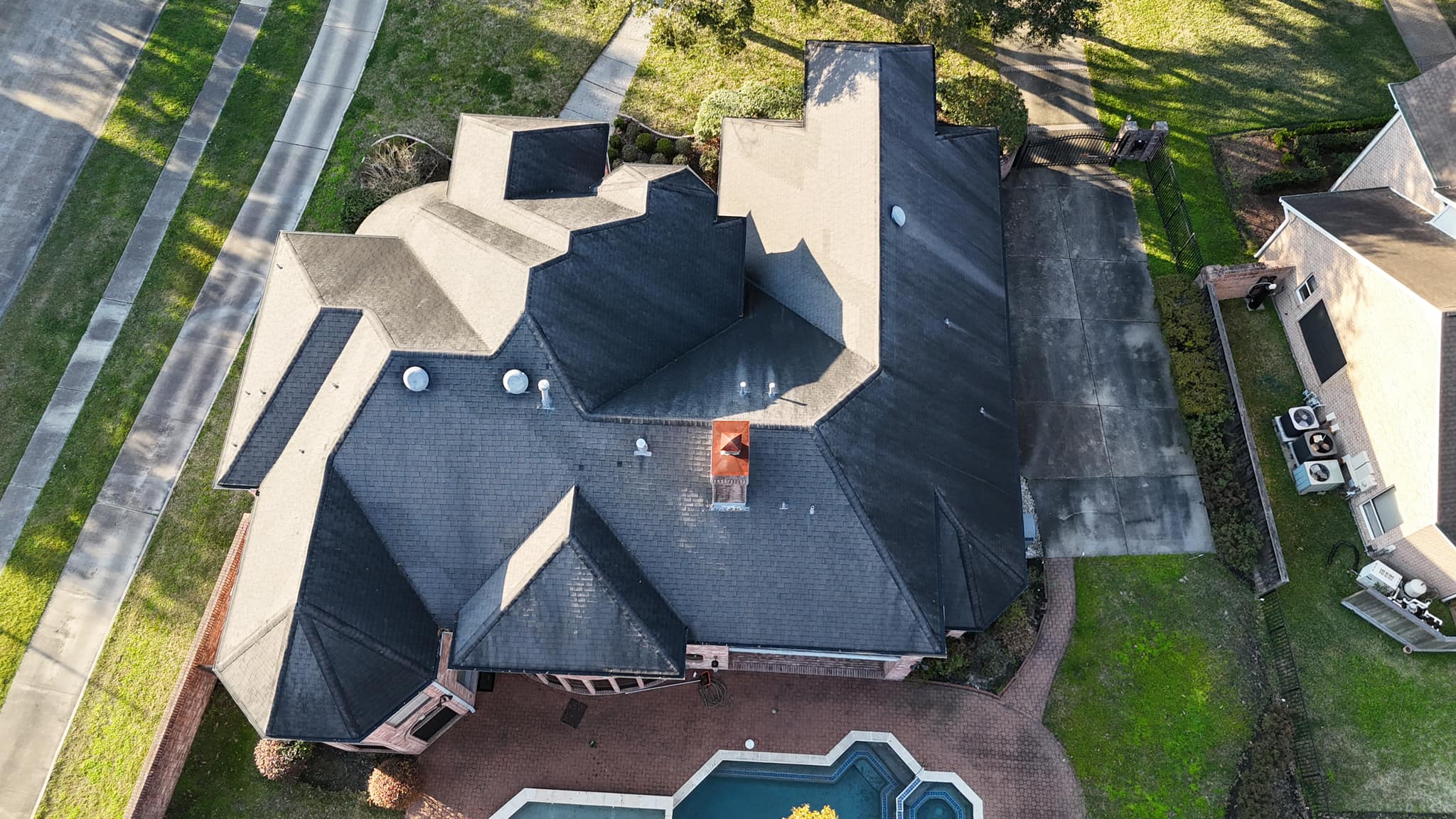 default Aerial view of a residential roof in Austin, Texas, showcasing dark shingles, a central chimney, and surrounding landscaping, highlighting the need for roof repair and maintenance services by Mr. Roof Fix.