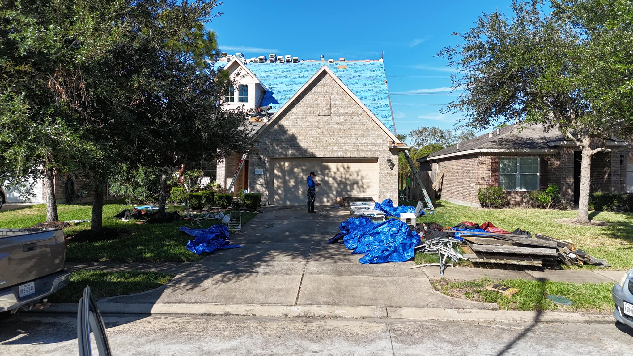 default Roof replacement in San Antonio, featuring a home with ongoing roofing work, blue tarps, and construction materials scattered around.